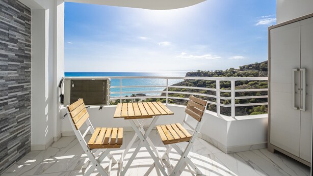 Un balcón con vista al mar, un armario blanco, y una mesa y sillas de madera.