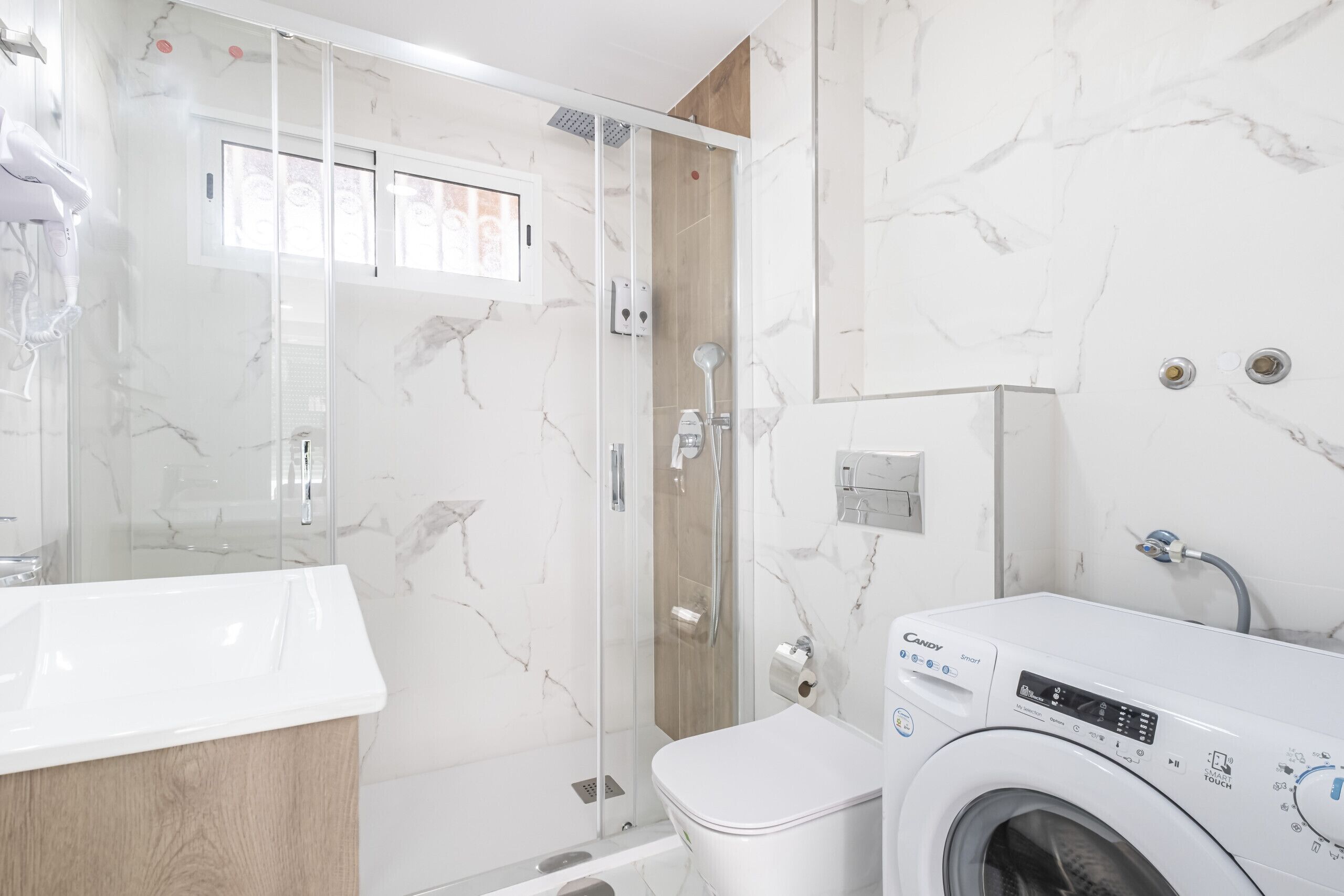 Ein modernes Badezimmer mit einer gläsernen Duschkabine, einem weißen Waschbecken und einer Frontlader-Waschmaschine.