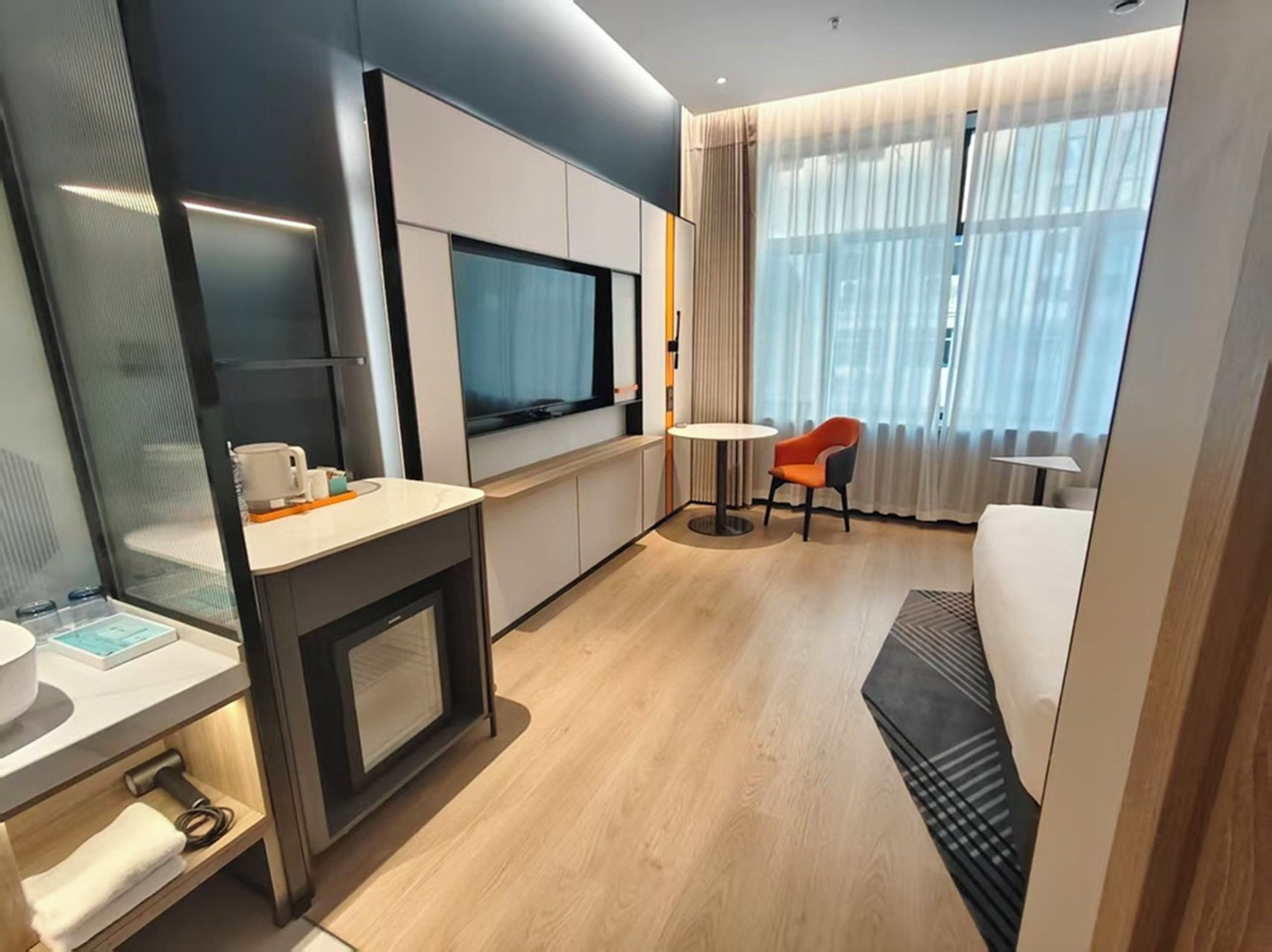 Une chambre d’hôtel moderne dotée d’une kitchenette, d’un téléviseur à écran plat, d’une table à manger ronde et d’un coin salon confortable offrant une vue sur la ville.