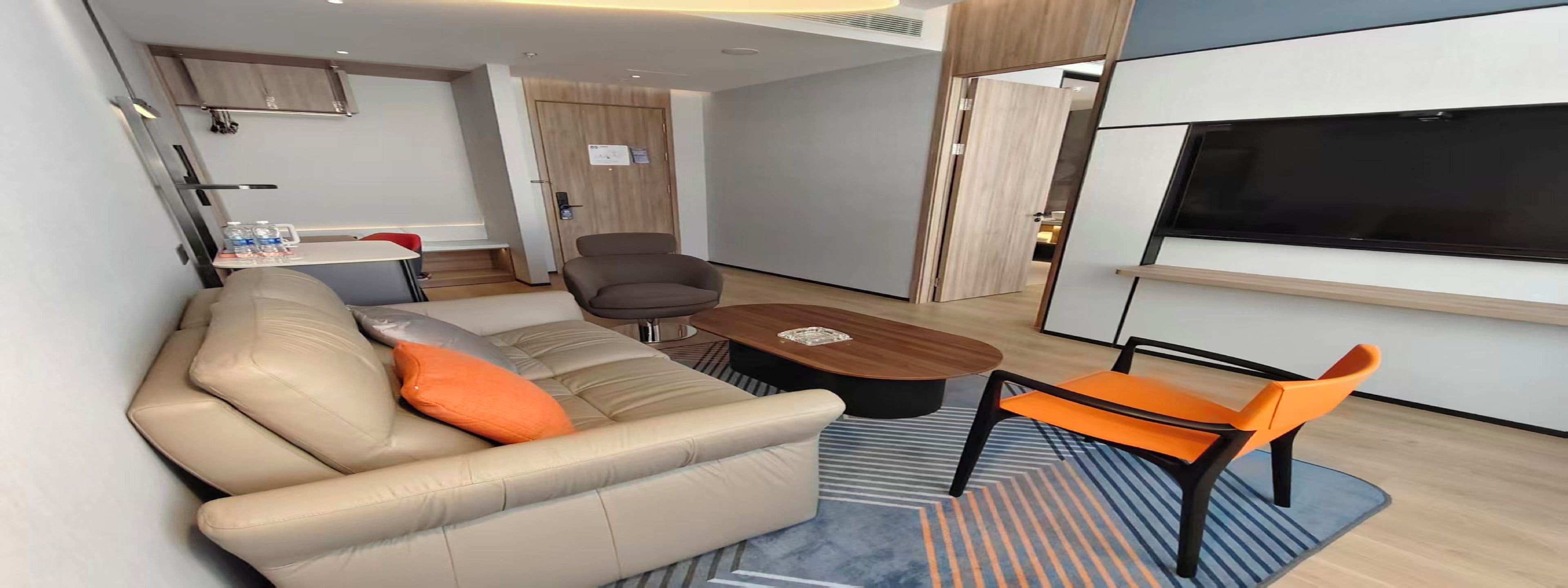 A modern living room with a sofa, armchairs, a coffee table, and a TV.