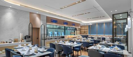 Un restaurante moderno con varias mesas, sillas y una cocina visible a través de paredes de vidrio.