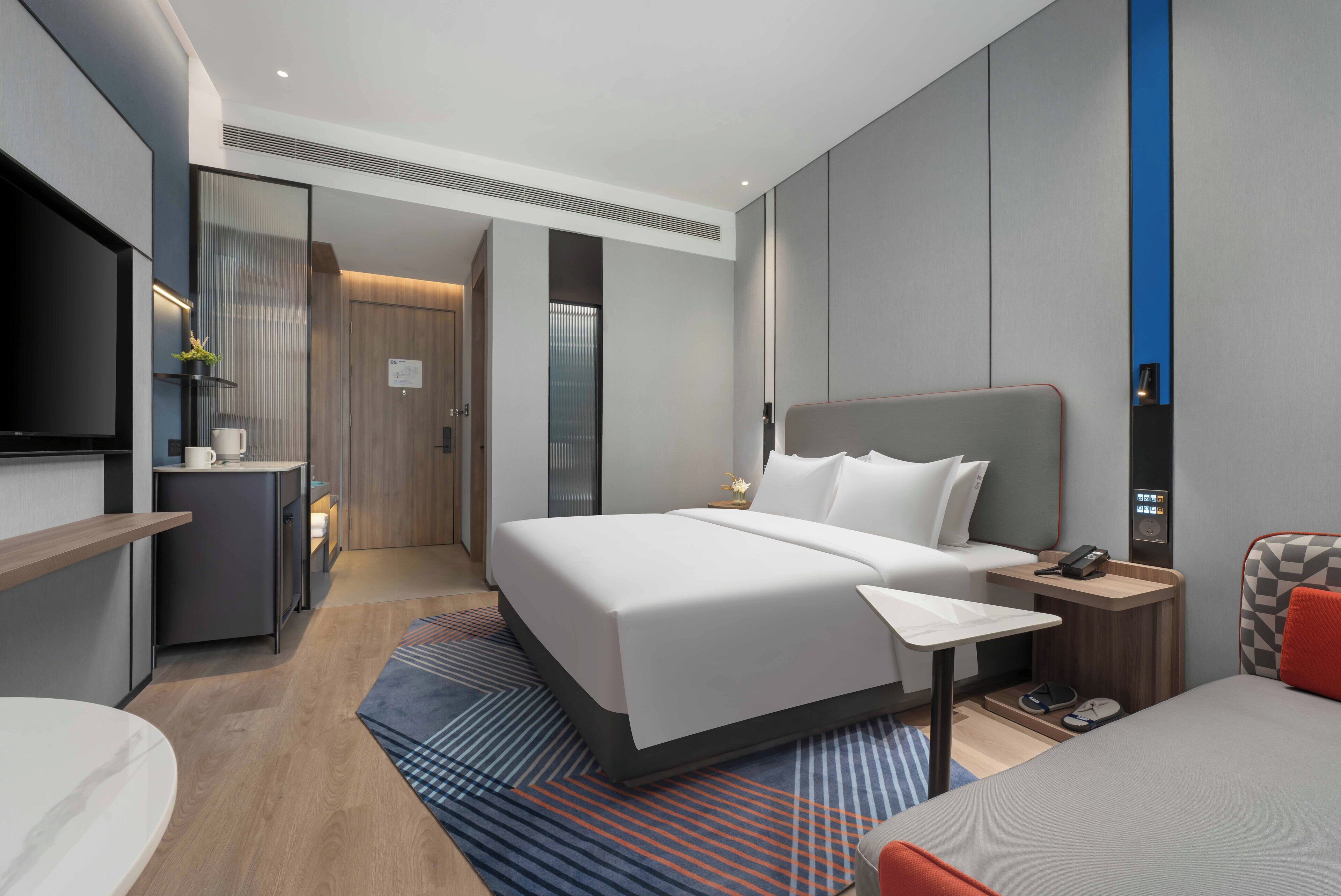 A modern hotel room with a large bed, bedside table, and a TV.