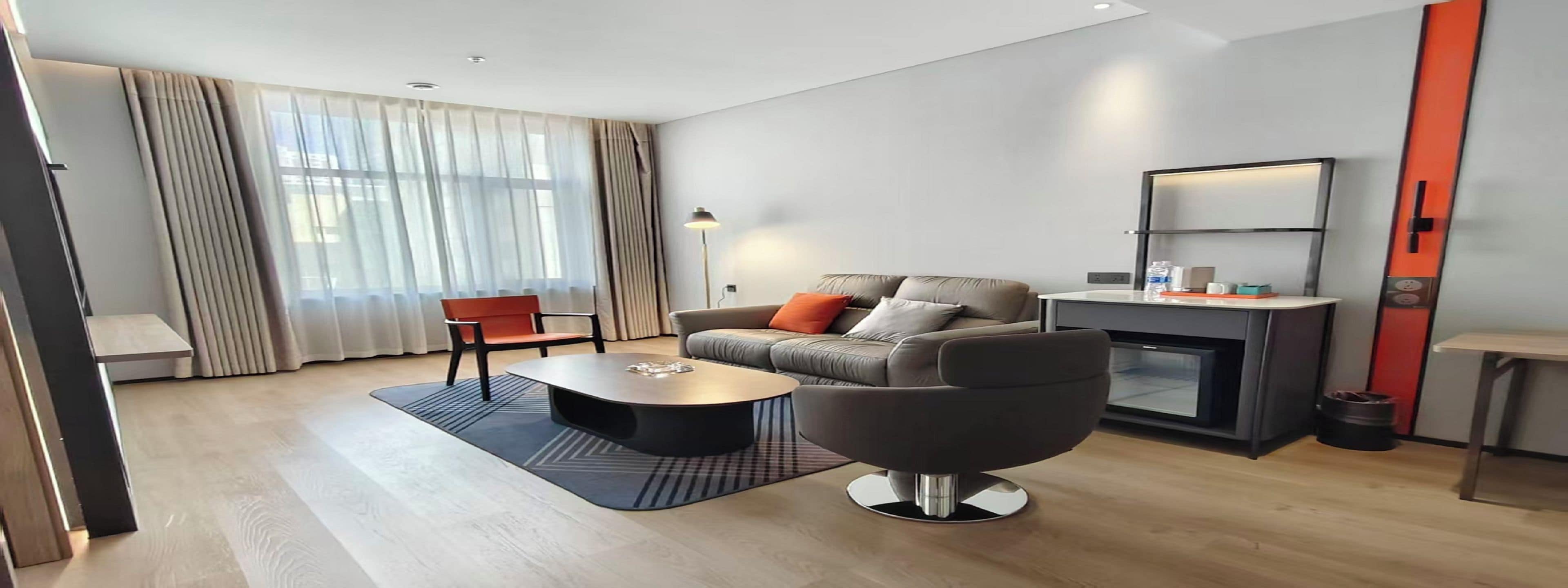 Una sala de estar moderna con un sofá, una mesa de centro y un sillón. Hay una chimenea, una lámpara y una ventana con cortinas.