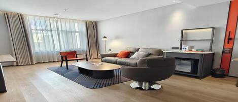 Una sala de estar moderna con un sofá, una mesa de centro y un sillón. Hay una chimenea, una lámpara y una ventana con cortinas.