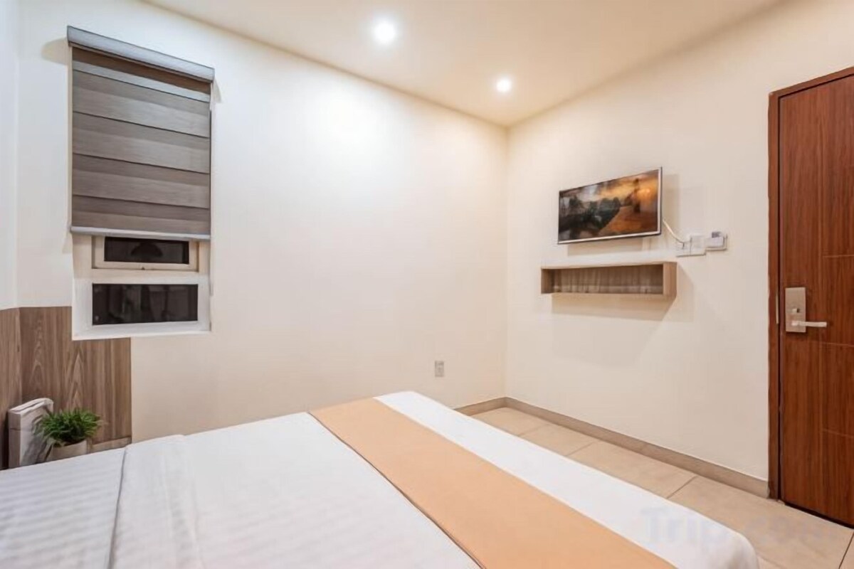 A bedroom with a bed, a window with blinds, a painting on the wall, and a door.