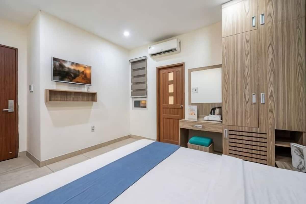 A bedroom with a bed, a desk, a chair, a wardrobe, and a television on the wall.