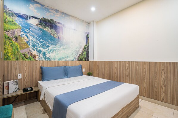 A hotel room with a large mural of a waterfall, a wooden headboard, a bed with blue bedding, and a nightstand with a remote control.