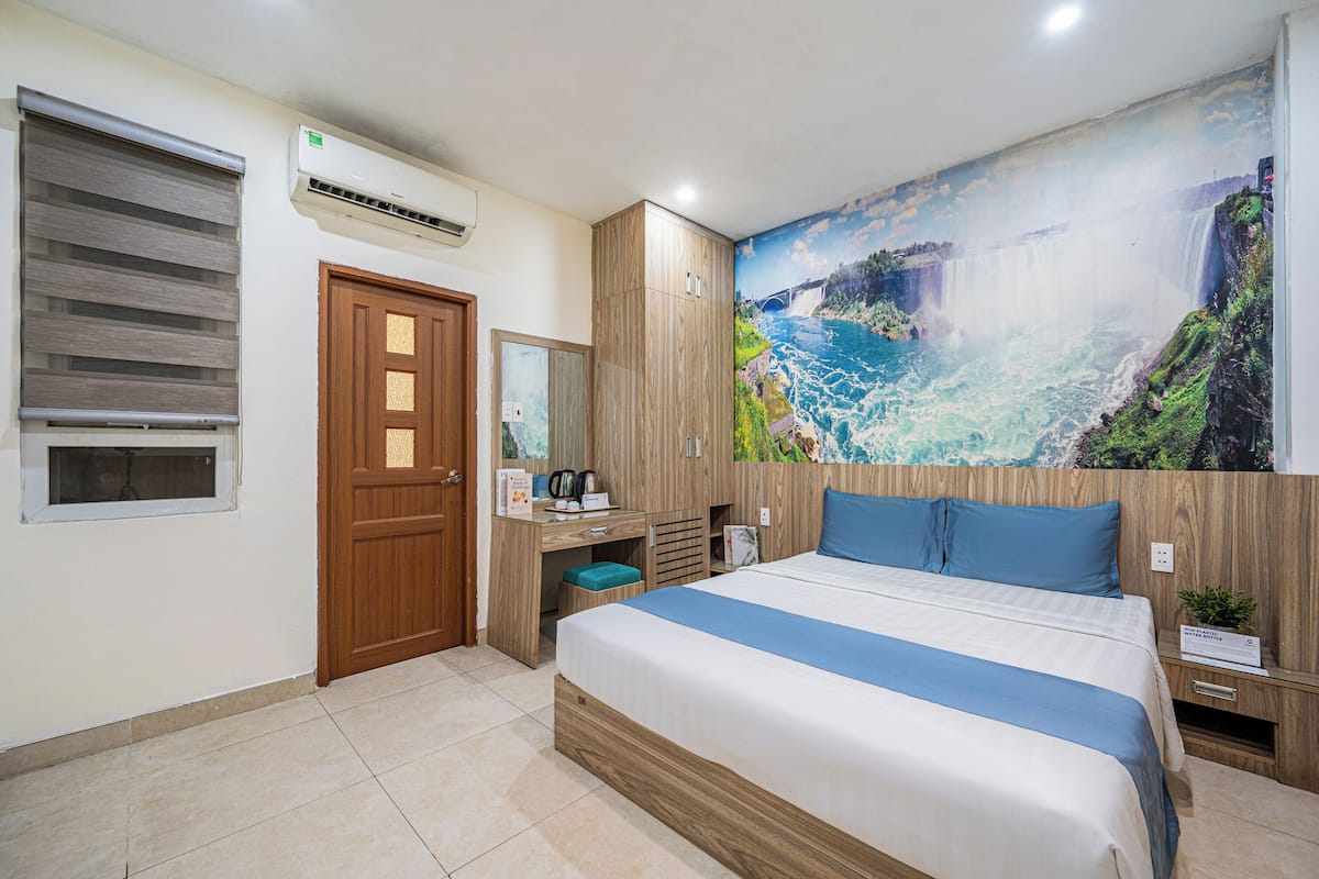 A hotel room with a bed, a desk, a wardrobe, and a large mural of a waterfall.
