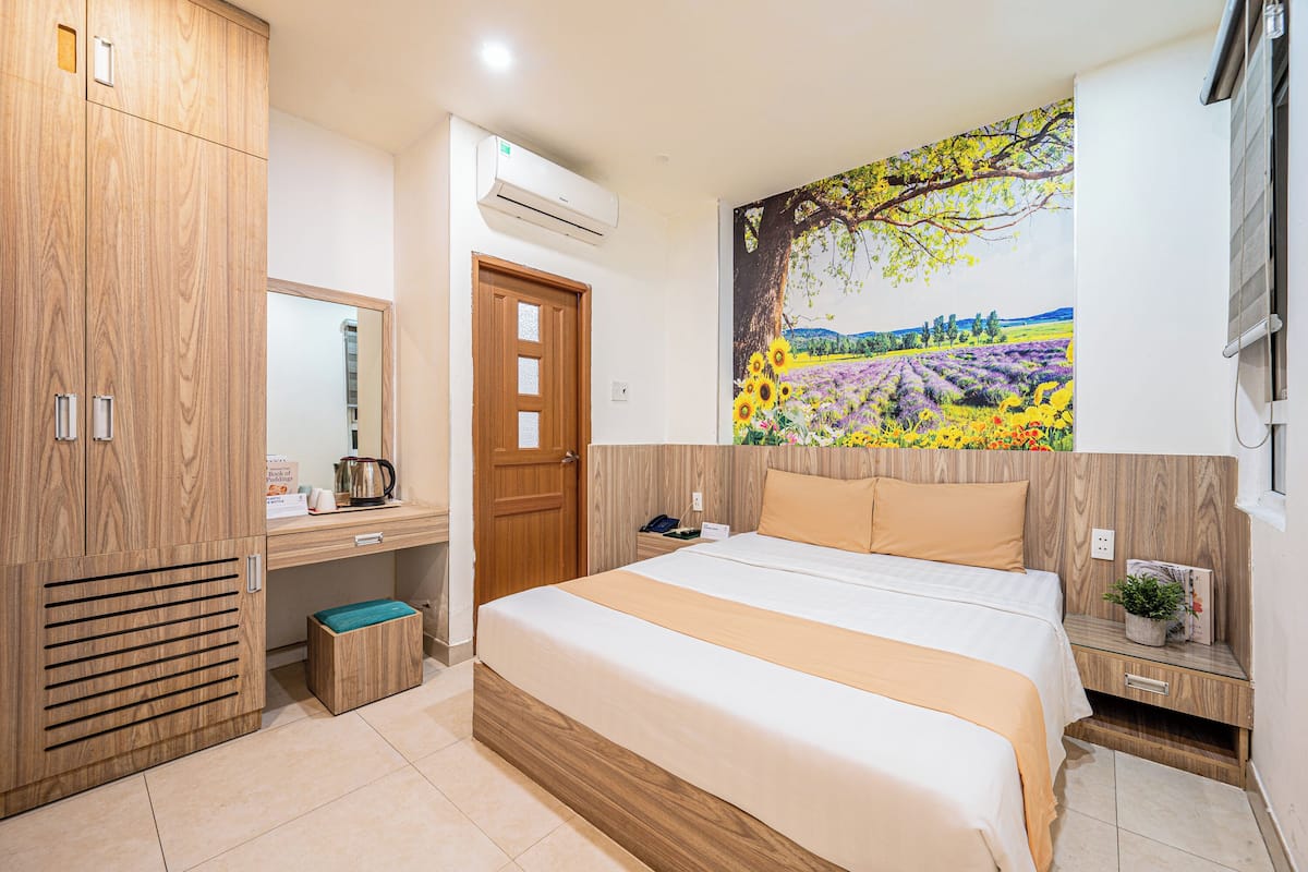 A bedroom with a bed, wooden wardrobe, a desk with a mirror, and a large painting on the wall.