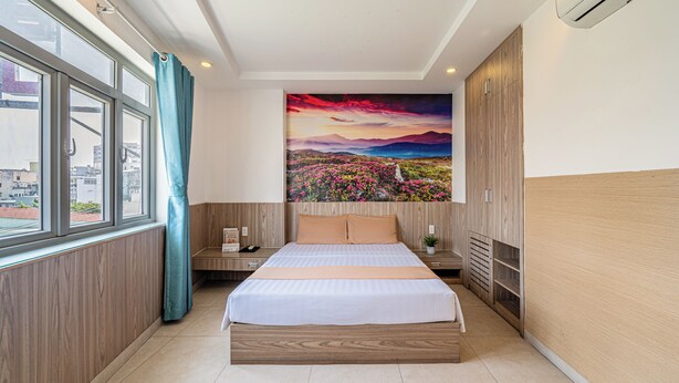 A hotel room with a large bed, a painting of a landscape, a window with curtains, and a wooden wardrobe. - Cozrum - Love Hotel Trần Bình Trọng (Ho Chi Minh City)