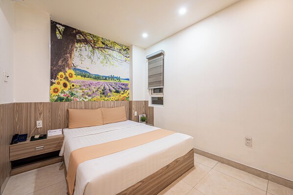 A bedroom with a large bed, a nightstand, a wall-mounted TV, and a window with blinds.