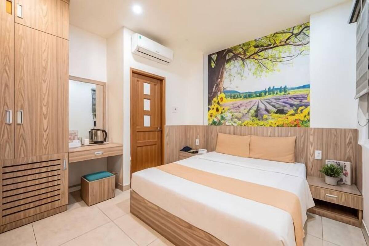 A bedroom with a bed, wooden wardrobe, desk, and a painting on the wall.