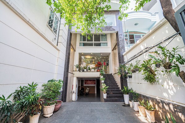 A narrow, covered walkway with potted plants on either side, leading to a building entrance with a staircase. - Cozrum - Love Hotel Trần Bình Trọng (Ho Chi Minh City)