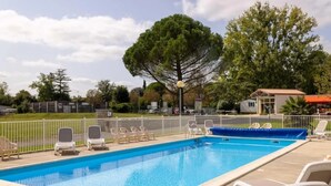 A rectangular swimming pool with a blue water surface, surrounded by a white fence. There are several lounge chairs and a small building in the background. - ZEcamping 3* animaux acceptés piscine et restaurant (Saintes)