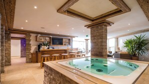 A spa area with a hot tub, wooden bar, stone walls, and a television. - Val Saraina Resort Apartments Lenzerheide (Lantsch-Lenz)