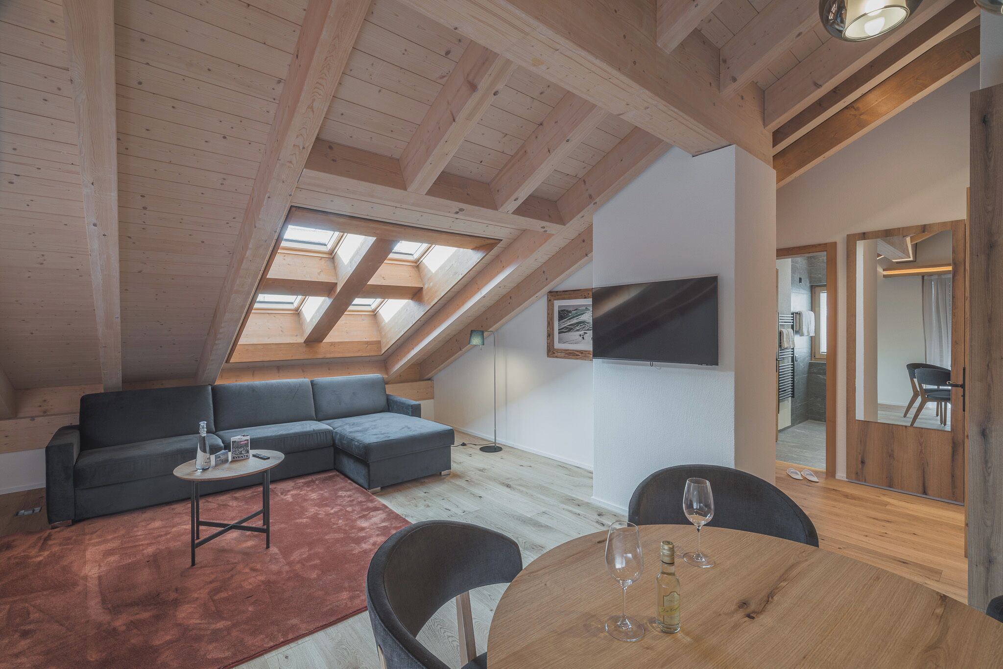 Un loft moderne avec un plafond en pente, un canapé d’angle gris, une petite table ronde et un coin repas avec des chaises.