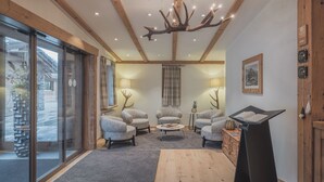 A cozy living room with a fireplace, comfortable seating, and a large window overlooking a snowy landscape. - Val Saraina Resort Apartments Lenzerheide (Lantsch-Lenz)