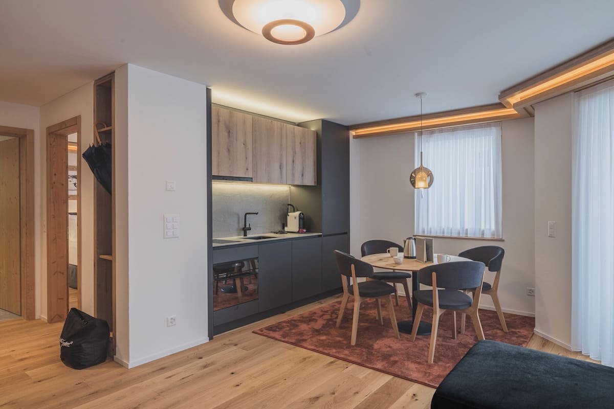 A modern kitchen with wooden cabinets, a dining area with a table and chairs, and a large window with curtains.