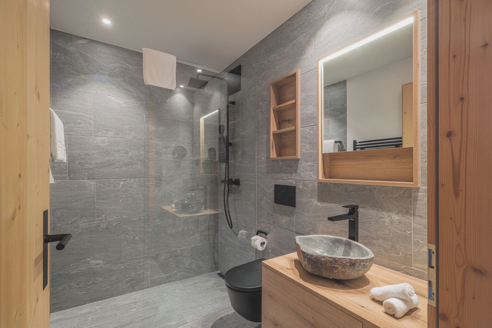 A modern bathroom with a glass-enclosed shower, a wooden vanity with a stone basin, and a large mirror.