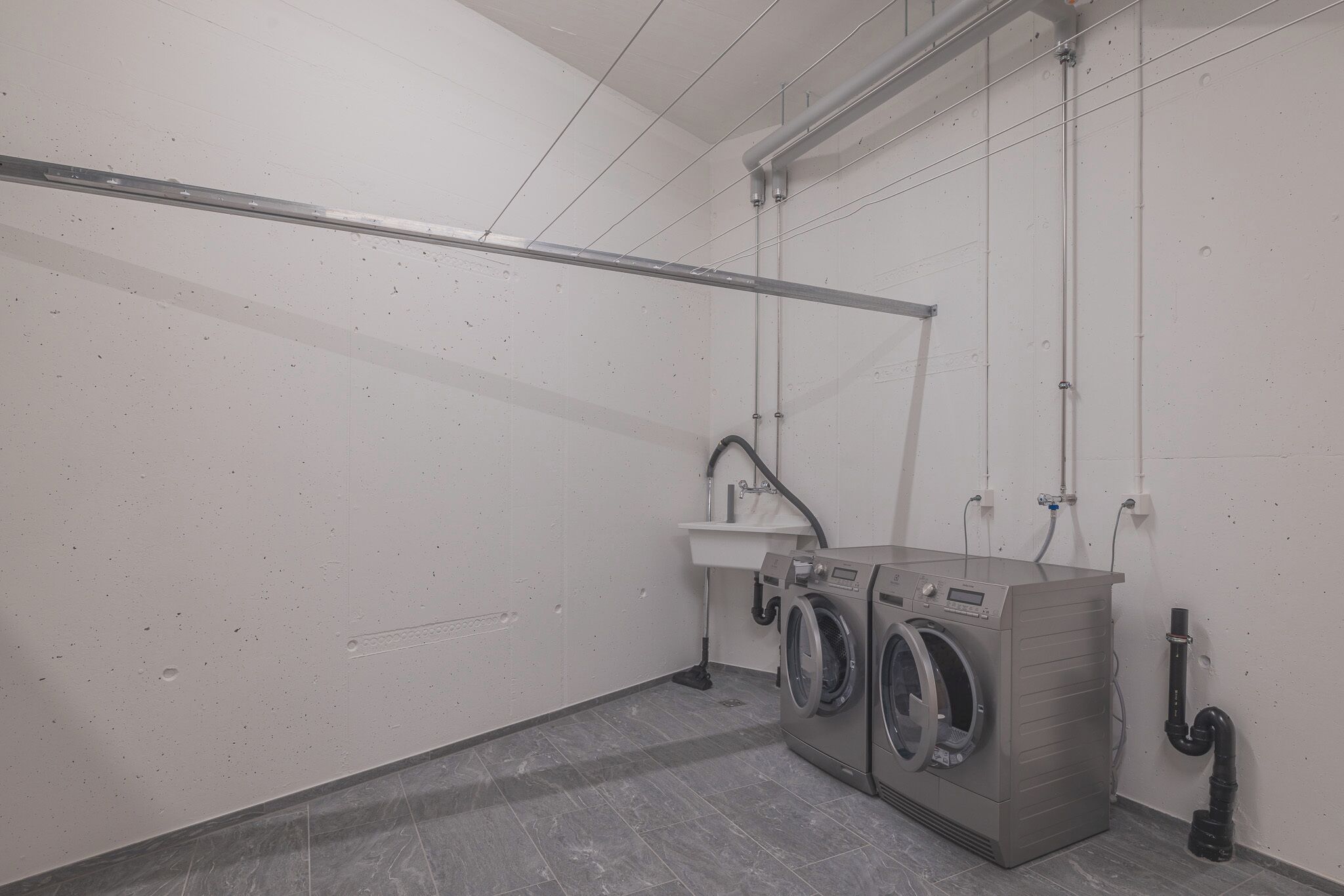 Une buanderie équipée d’un lave-linge, d’un évier et d’un tuyau d’eau.