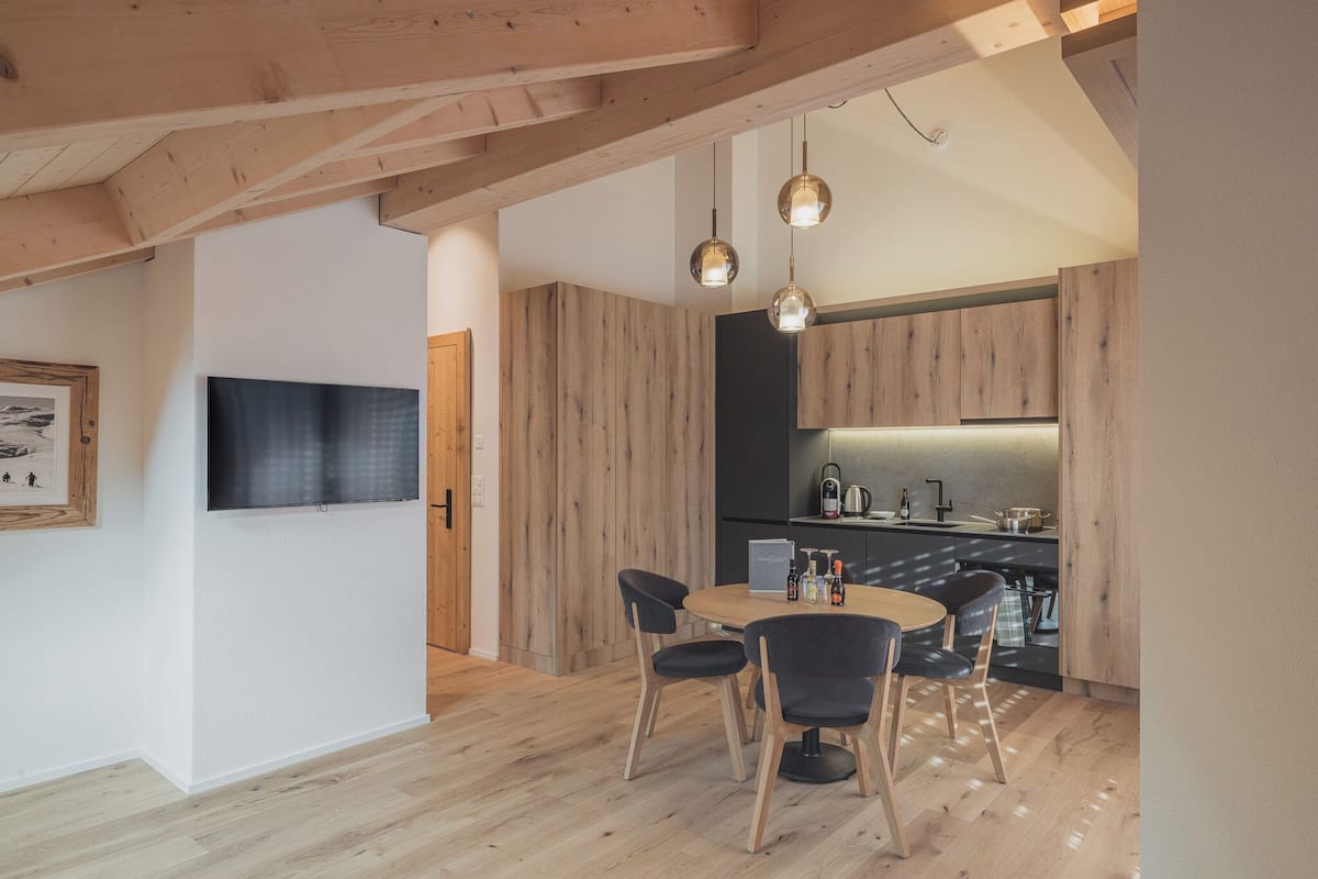 A modern kitchen with wooden cabinets, a dining area with a round table and chairs, and pendant lighting.