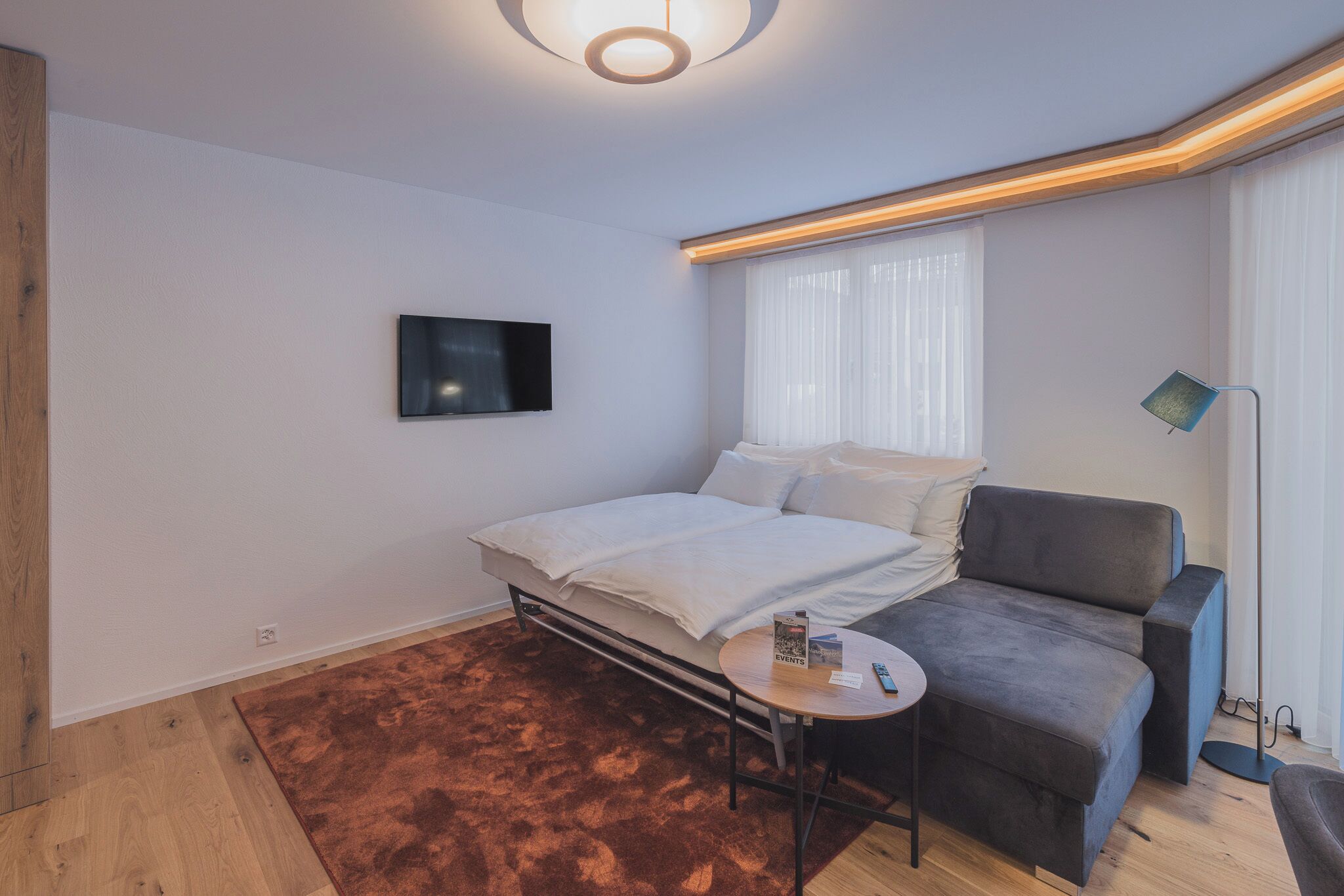 Un dormitorio moderno con cama, sofá, una mesita y televisor.
