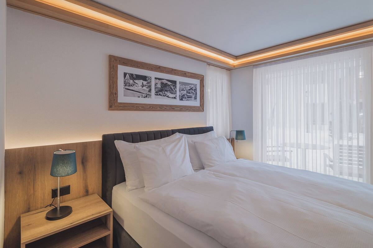 A neatly made bed with white linens, a wooden nightstand with a lamp, and a framed picture on the wall.