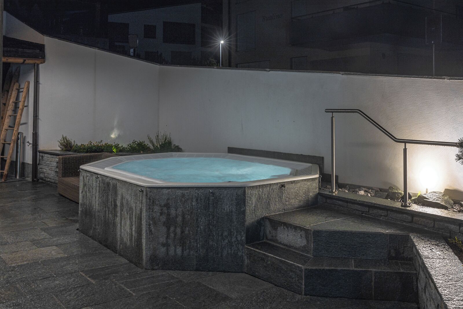 Ein Whirlpool im Freien mit Stufen, umgeben von Steinmauern und einem Geländer.
