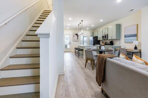 A modern kitchen with a central island, a dining area with a round table, and a staircase leading to another level. - Landing | Stylish 2BD, Clubhouse, Gym (Leland)