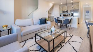 Een moderne woonkamer met een bank, salontafel en een trap die leidt naar een keuken.