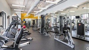 Un gimnasio con equipo de ejercicio diverso, espejos y una pared amarilla.