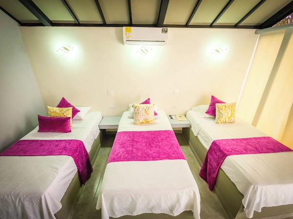 A hotel room with three single beds, each with a white mattress and a pink blanket. There is an air conditioning unit above the beds, and a small table between them with a phone and a book. - NEW STAR CENTER (Rionegro)