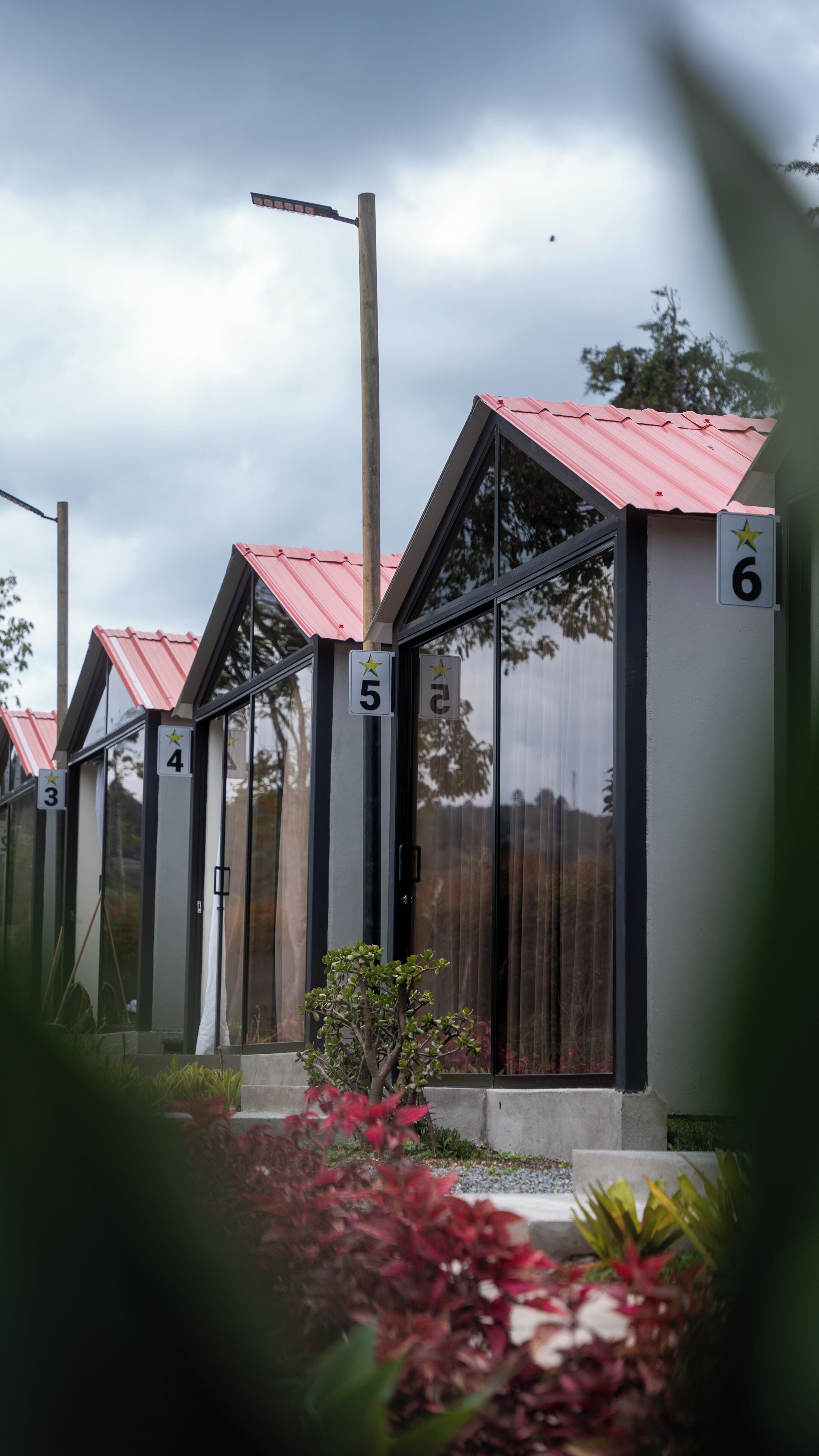 A row of modern, numbered cabins with red roofs and large windows, set against a cloudy sky.
