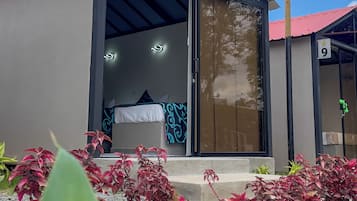 Um edifício moderno com entrada por porta de vidro, com os números 8 e 9, e uma pequena área ajardinada com plantas de folhas vermelhas em primeiro plano.