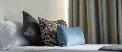 Una cama con tres almohadas, una blanca lisa, una gris oscura y una multicolora con estampado floral.