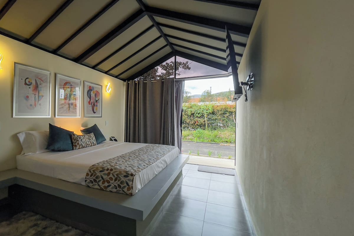 Un dormitorio con cama, almohadas, obras de arte y vistas a zonas verdes.