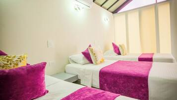 A hotel room with two beds, each with a white mattress and purple bedspreads. There is a ceiling fan and an air conditioning unit mounted on the wall.