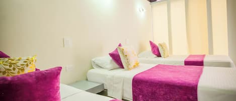 A hotel room with two beds, each with a white mattress and purple bedspreads. There is a ceiling fan and an air conditioning unit mounted on the wall.
