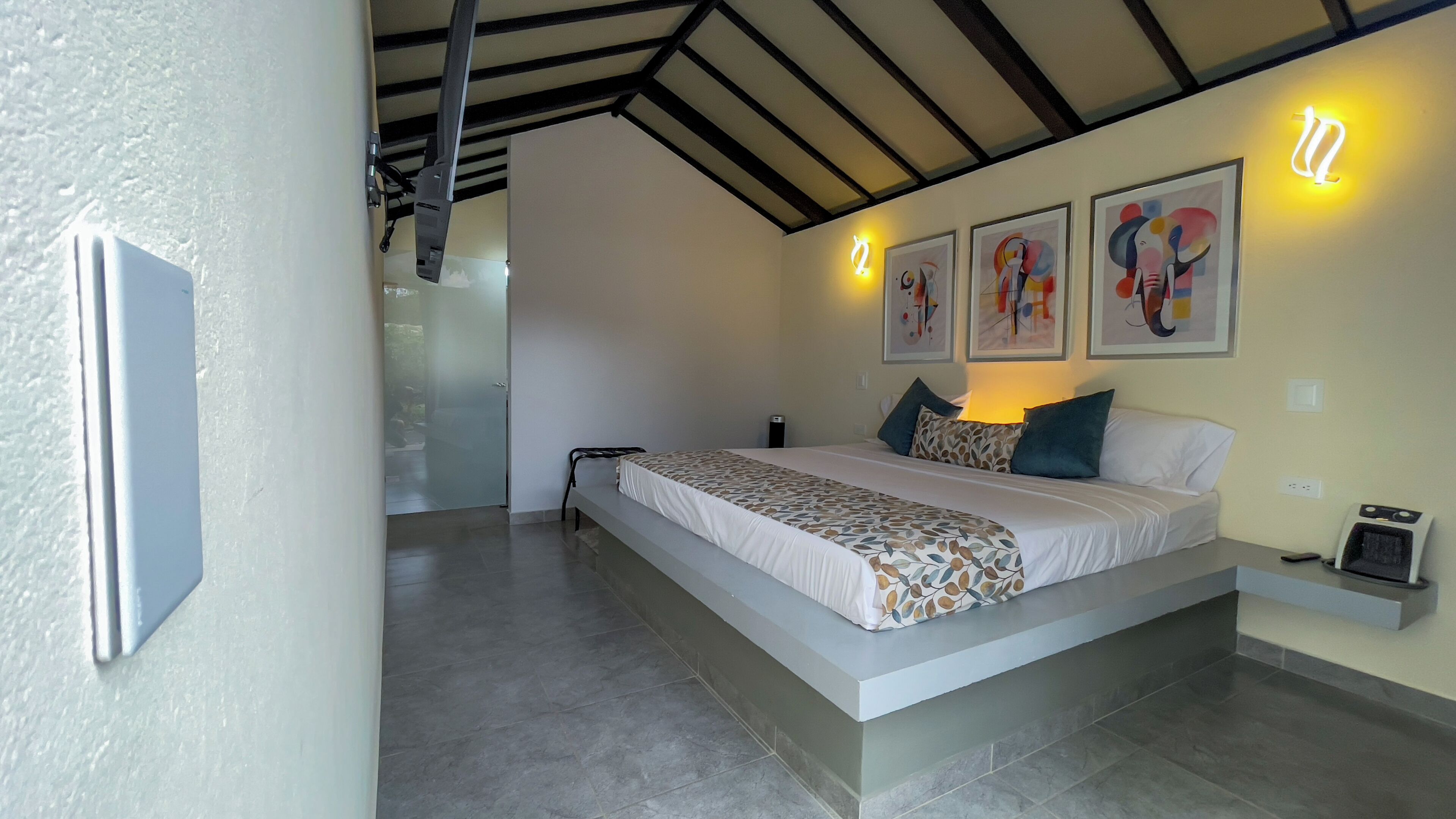 A modern bedroom with a large bed, a ceiling fan, and abstract wall art.