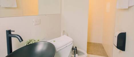 Un baño moderno con un lavamanos ovalado grande, un espejo, un perchero para toallas, un inodoro y un secador de manos.