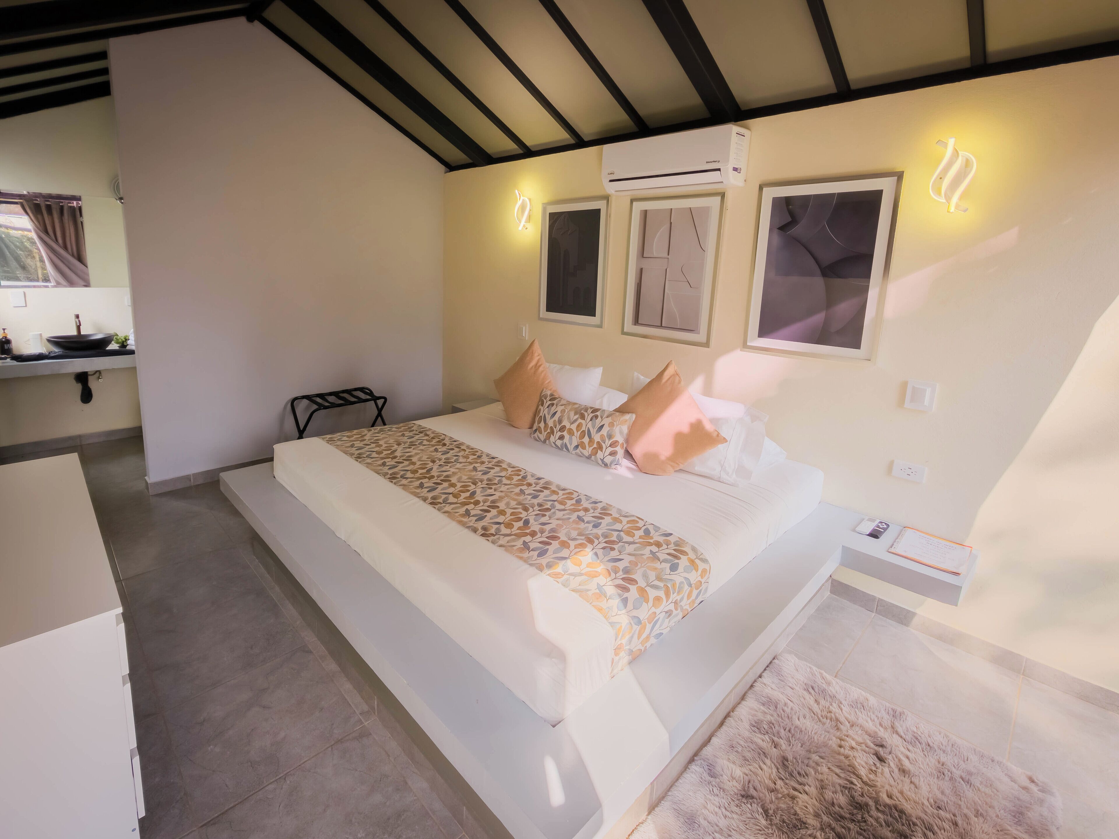 A hotel room with a bed, bedside table, air conditioning unit, and a window with curtains.