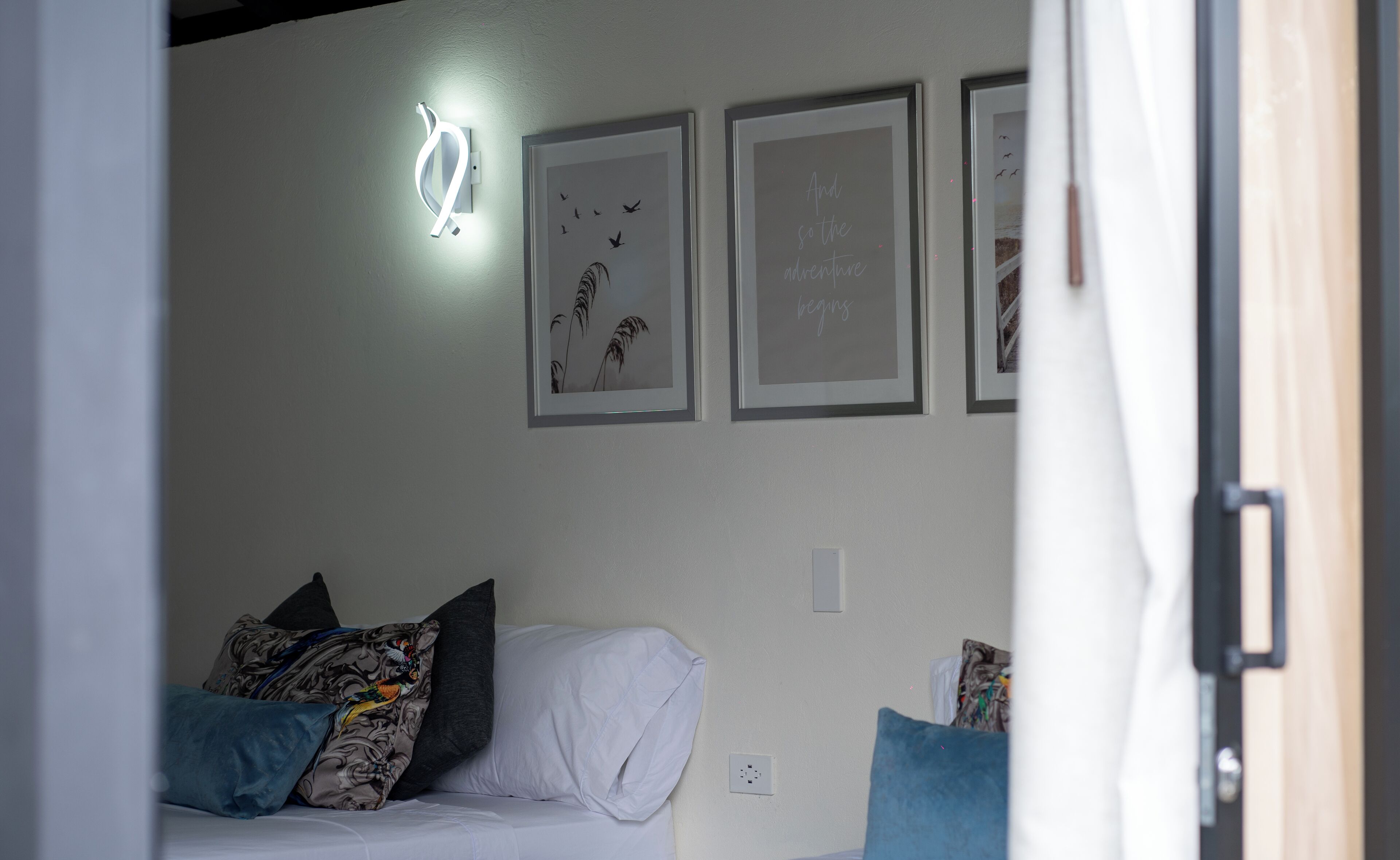 A bedroom with a bed, pillows, a wall-mounted light, and framed pictures.