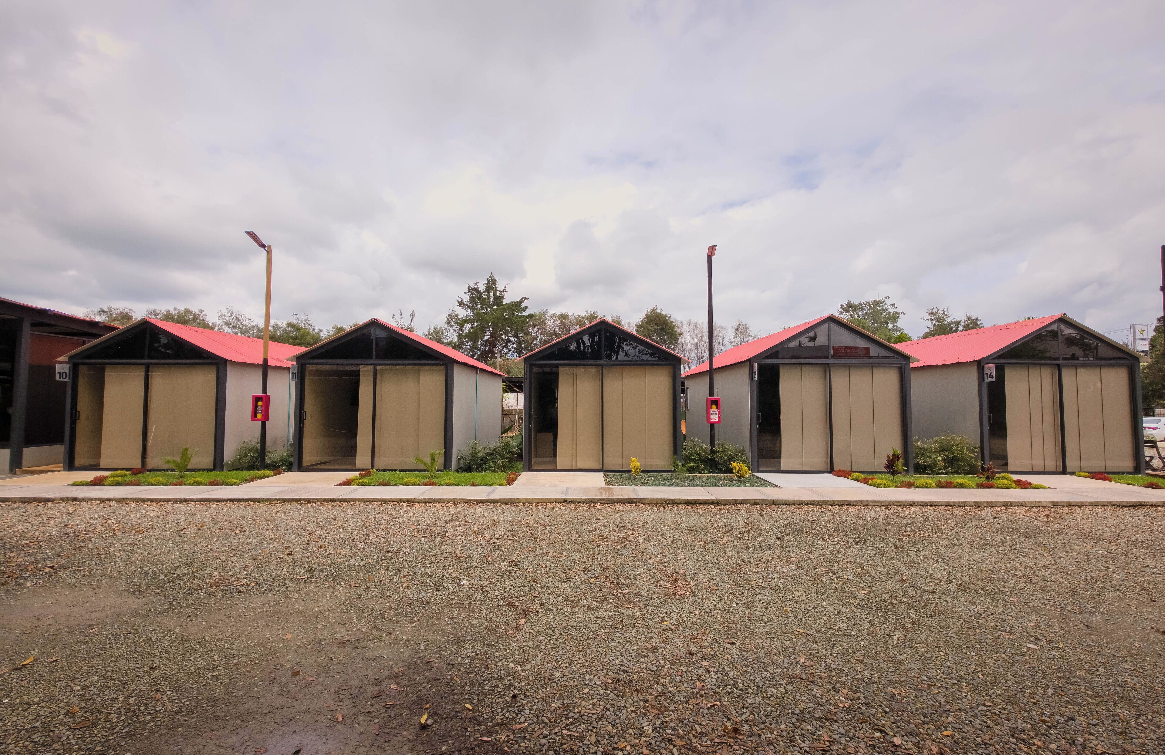 A row of identical buildings with red roofs and beige walls, numbered 10 to 14, with small gardens in front.