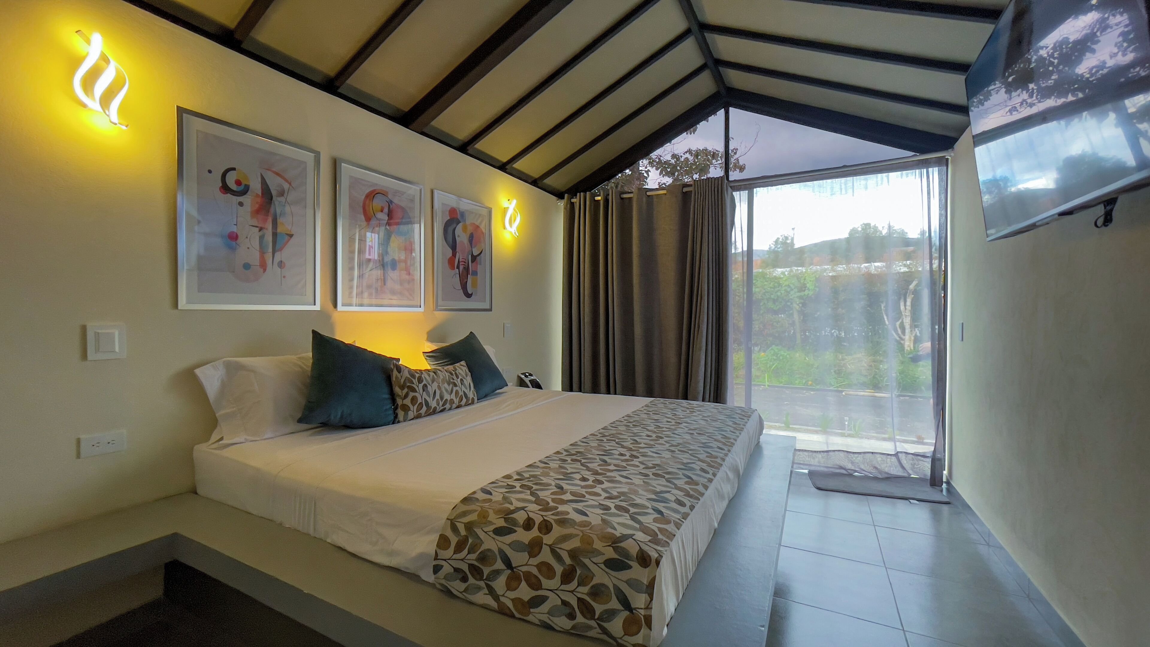 Una habitación de hotel con cama, televisión y obras de arte en la pared.