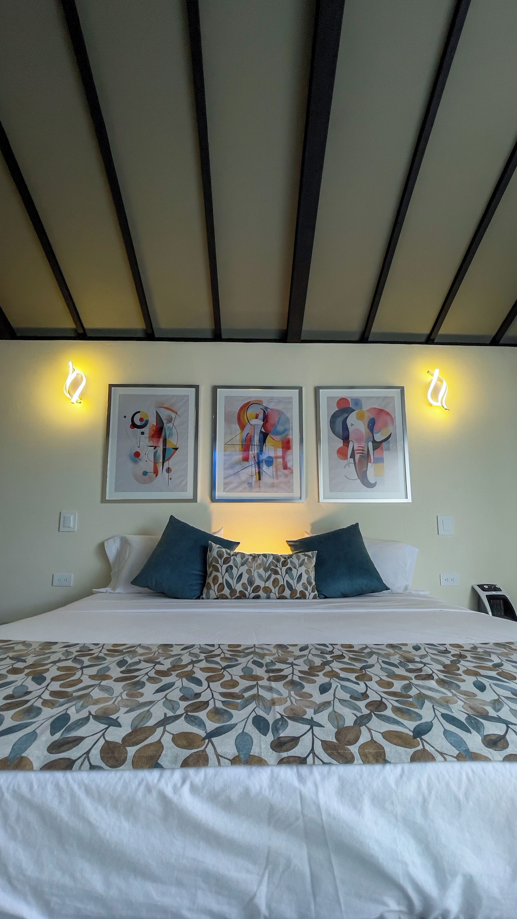 A bedroom with a bed, pillows, and wall-mounted artwork.
