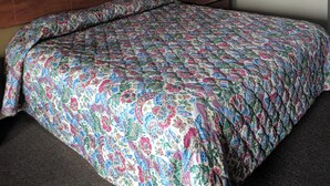 A hotel room with a large bed, a wooden headboard, and a plain wall. - BUDEGT MOTOR LODGE (New Castle)