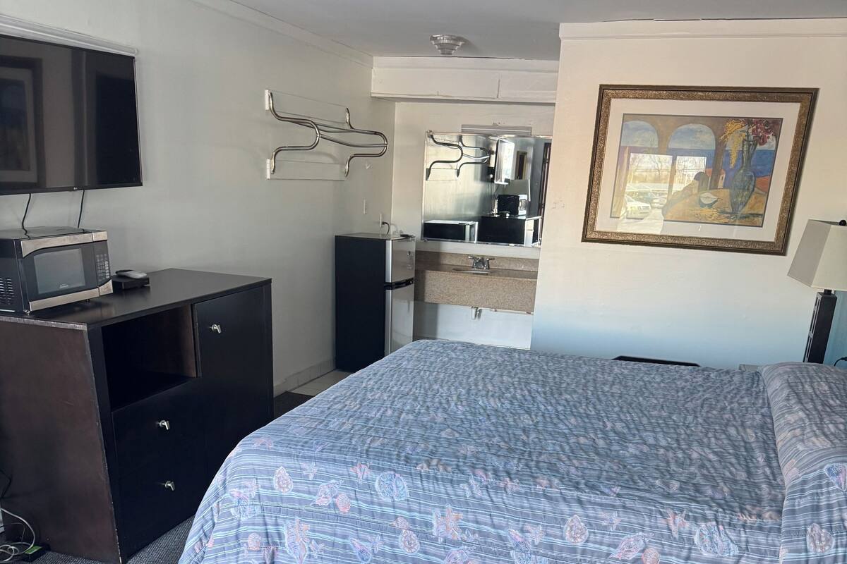 Una habitación de hotel con una cama, un escritorio con computadora, un microondas y un refrigerador.