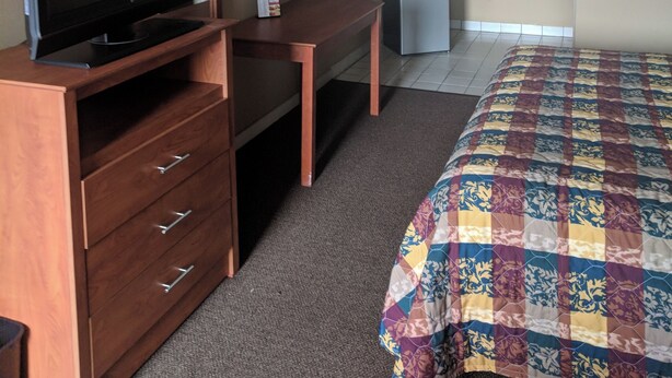 A hotel room with a wooden desk, a television, a bed with a colorful quilt, a kitchenette, and a bathroom with a mirror. - BUDEGT MOTOR LODGE (New Castle)