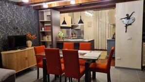 A modern living room with a dining area, featuring a TV, orange chairs, a wooden cabinet, and a kitchen in the background. - CASA "INCANTO" Charming house with breathtaking views of Lake Como. (Comun)