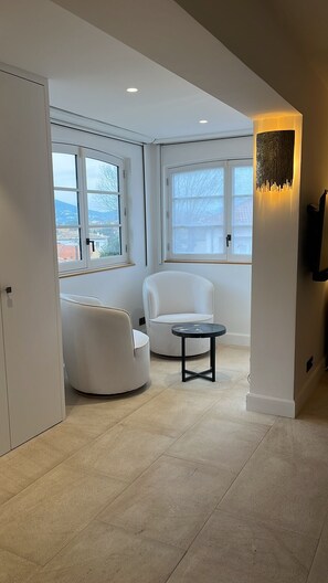 Una sala de estar moderna con un sofá blanco, un sillón redondo y una mesita. Hay ventanas grandes con vistas al exterior.